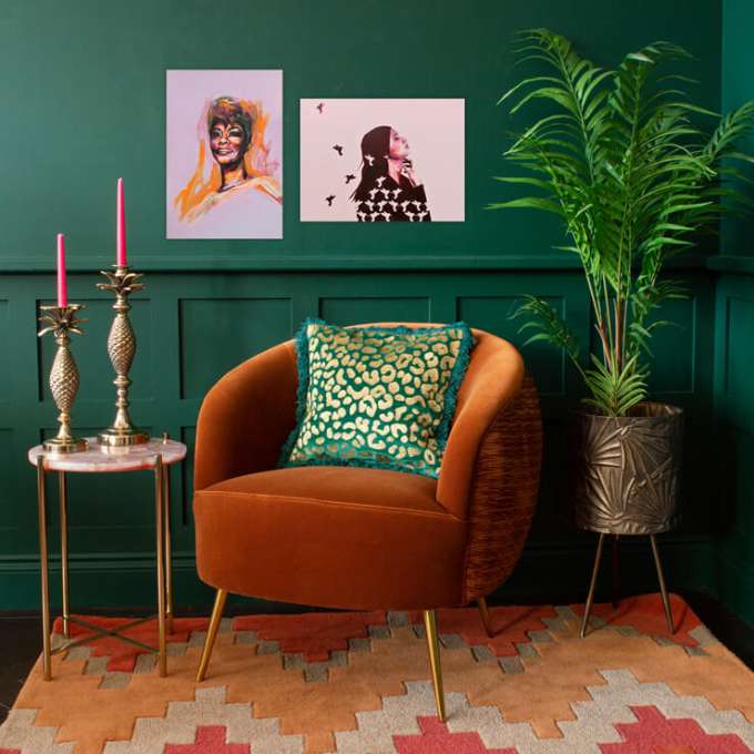 Burnt orange arm chair and a pillow with golden details on it and green backdrop