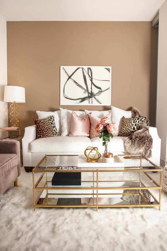 A white sofa with throw pillows on it an a gold framed coffee table with the glass top