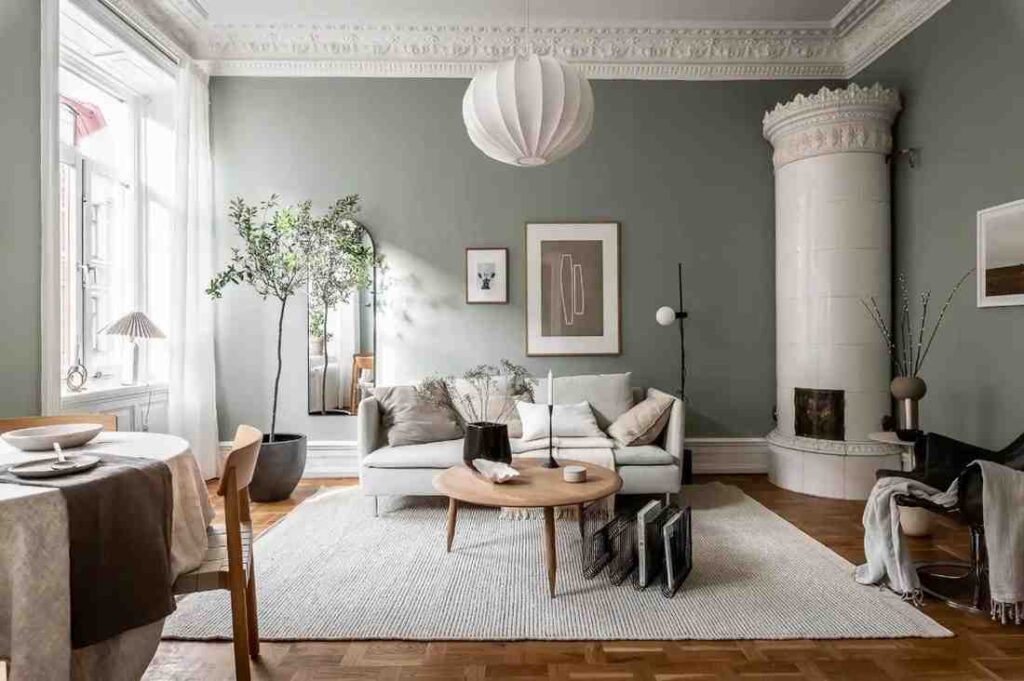 Sage green wall with a corner round fireplace and a wooden table in a center on beige carpet