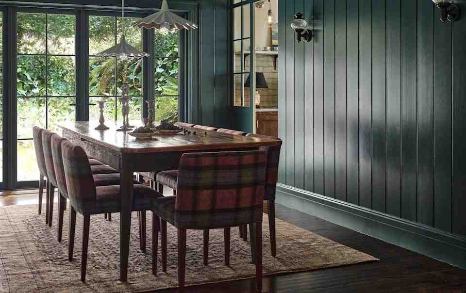 Dark teal colored wall panelling with checked chair and wooden table and dark wood floor