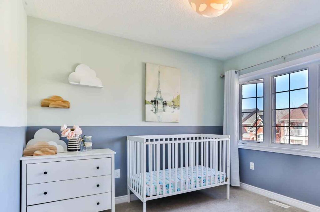 Two toned walls in blue and white color with a white color crib and a wooden cabinet for toddler room