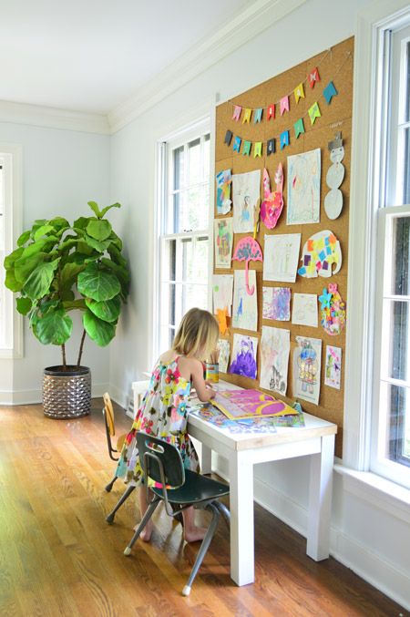 A cardboard bulletin board with drawing on it and a girl standing in front of it