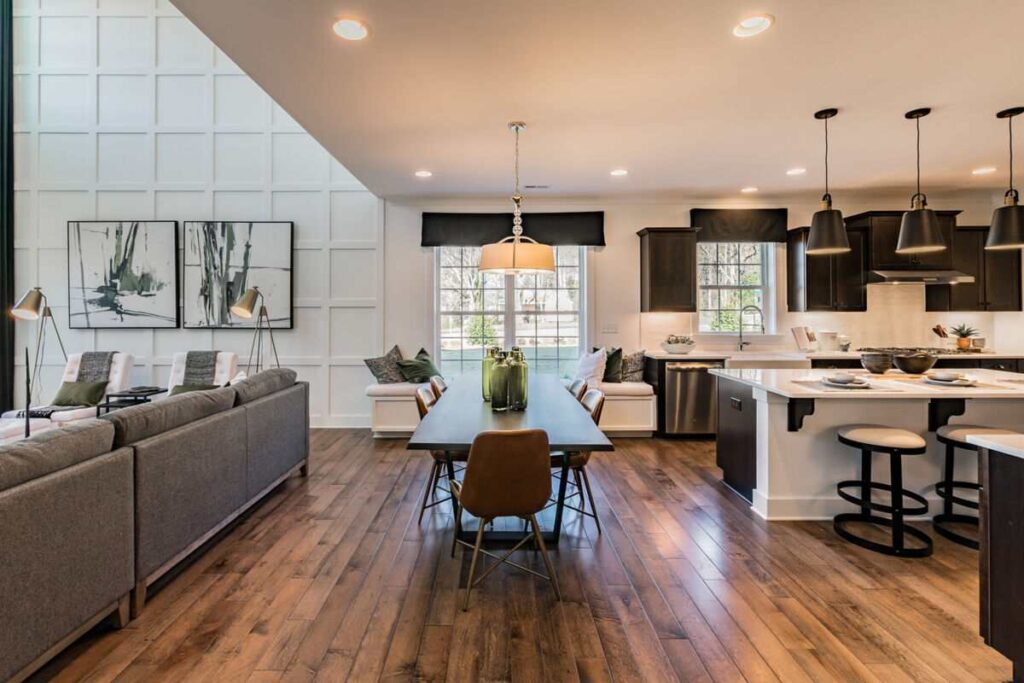 White wall panelling and a gray sofa and dining table with white counter top and laminate flooring