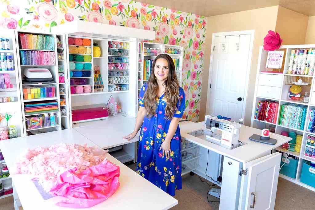 A lady standing in U shapes sewing table for sewing room with wall storage for fabric and other items