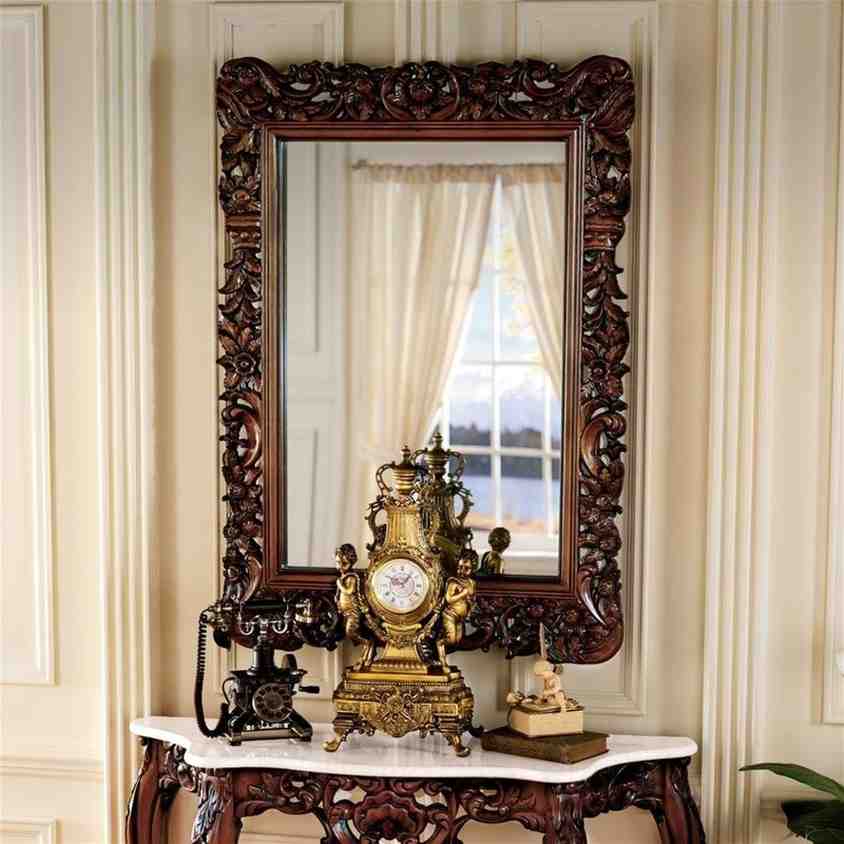 Wooden baroque mirror and a wooden table with marble top and telephone placed on it