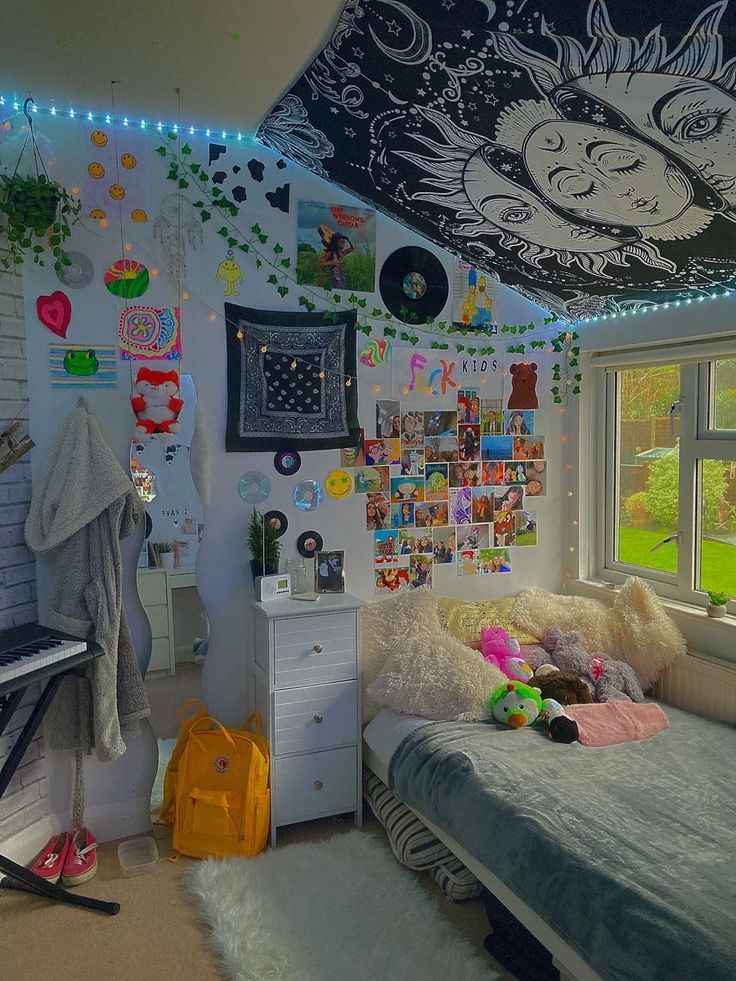 A wooden white cabinet and murals on wall with a black boho tapestry and window side bed