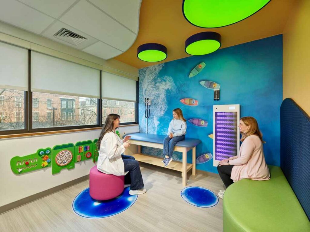 An ocean accent wall and a green sofa with kid and doctor seating in the room