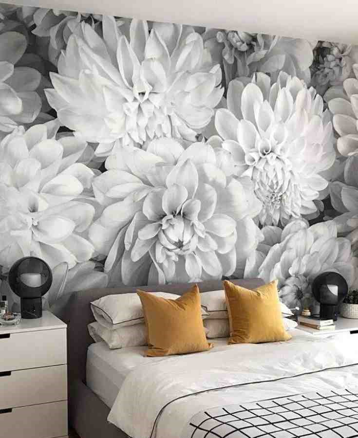 Grey and white floral print wallpaper as a backdrop and two yellow pillow on the bed with white bedsheet