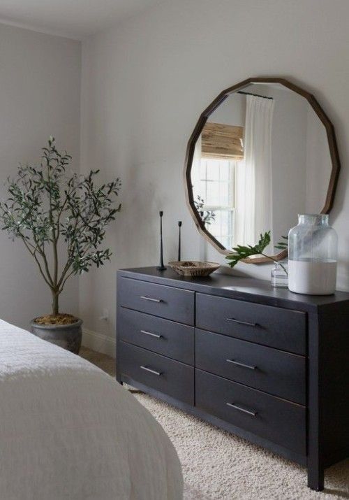 Round brass color mirror above the black cabinet and a plant in the corner of the room