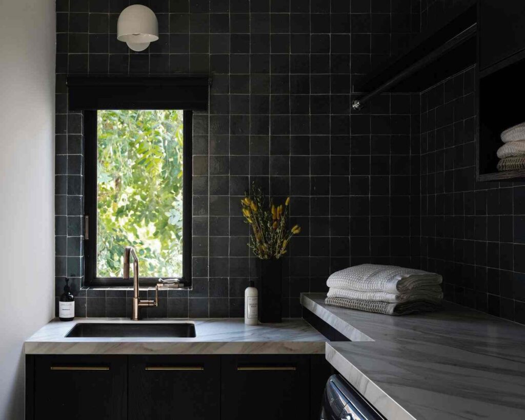 Black backsplash with tiles and white marble counter top in laundry room