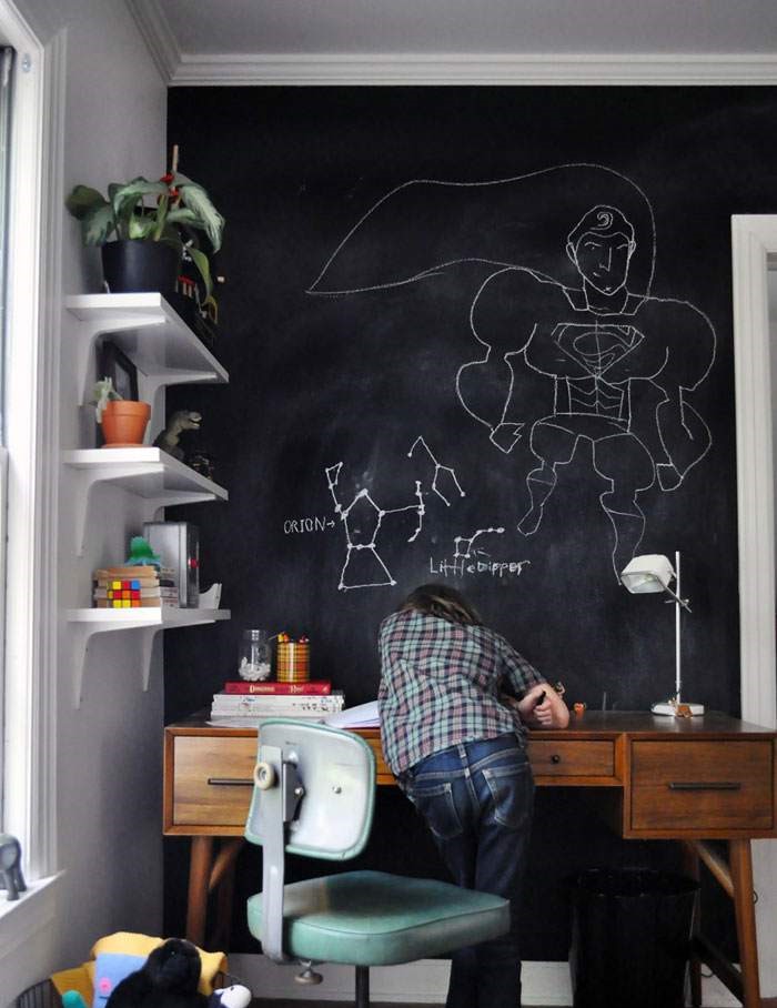 Chair and a wooden table with a kid standing and a chalkboard wall