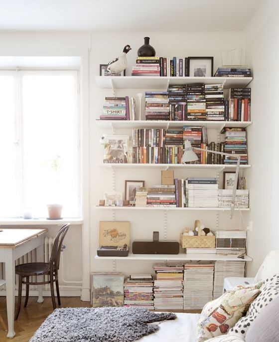 White floating shelves with books on them and a white bed and a lamp