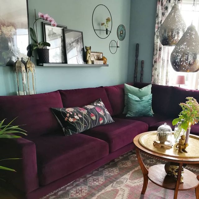 Black floating shelve with multiple frames on it and a burgundy sofa