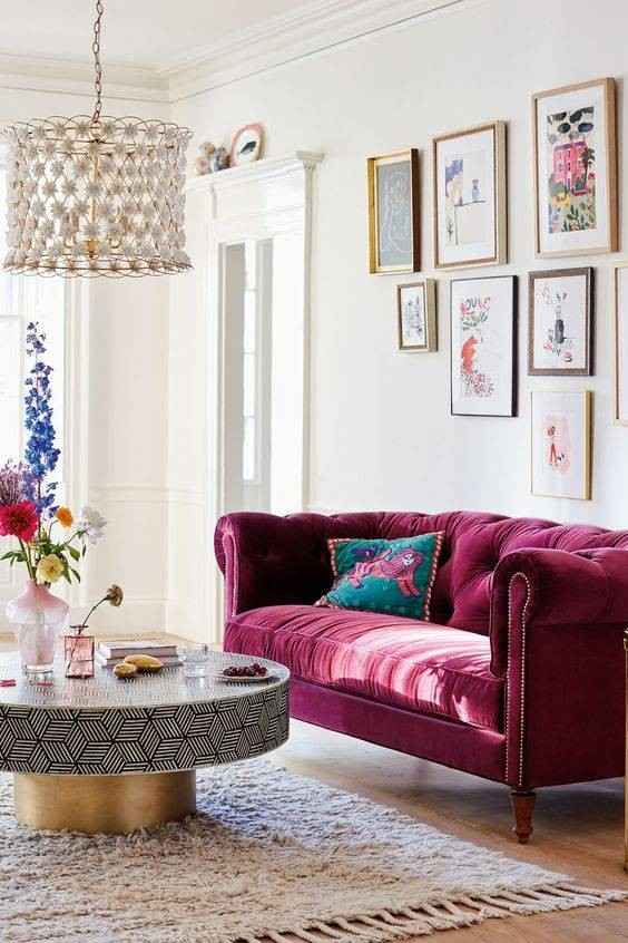 Golden and black patterned coffee table and a burgundy sofa with a white wall with art frames hanging on it