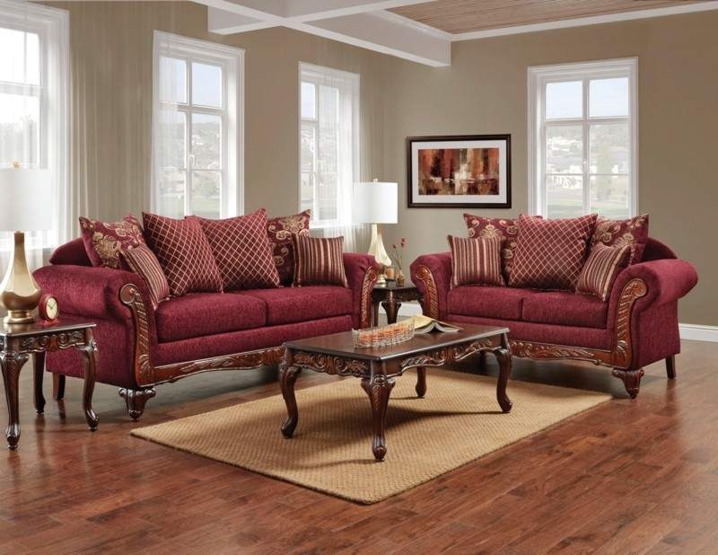 Golden and burgundy color throw pillows on burgundy sofa and a wooden coffee table in center