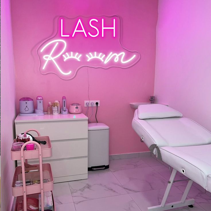 A white lash bed and a pink neon sign with brand name on pink wall and a white cabinet 