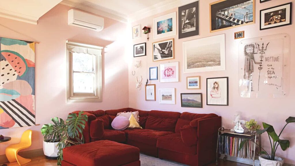 Pink wall with art frames hanging and burgundy sofa
