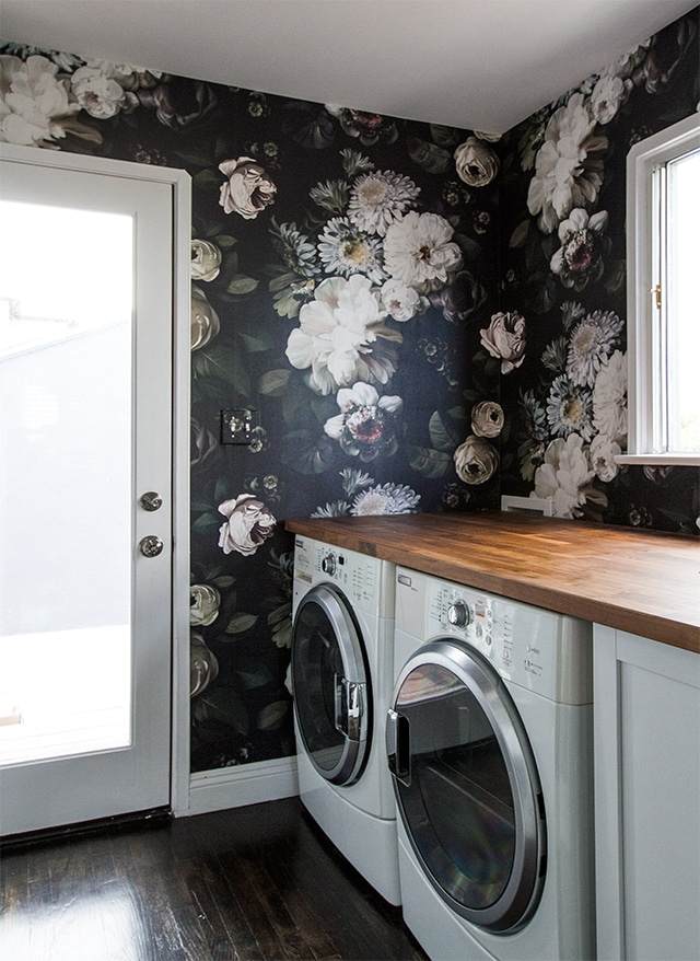 Wooden counter top with two white washing machine and black floral wallpaper