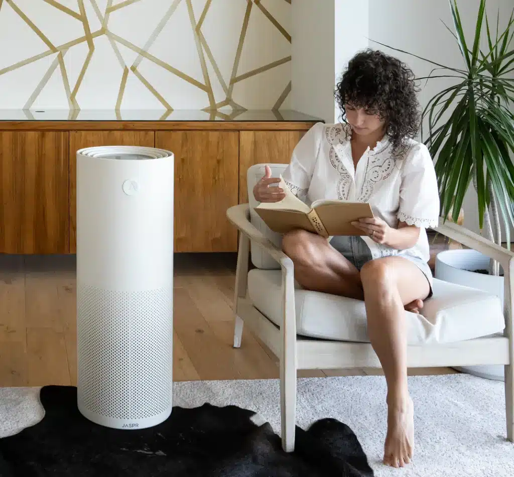 White tower air purifier and a lady seating on chair reading magazine