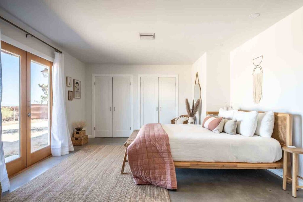 Wooden bed frame and white duvet on it and two door and white wall