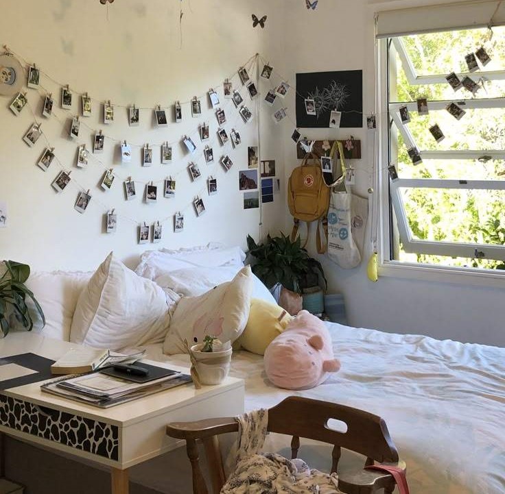 White duvet bed and stuff cushion on it with a side table and a polaroid's on wall