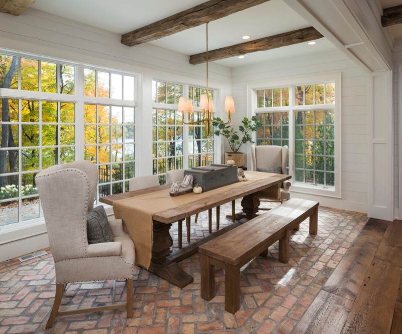 wooden exposed beams and a dining table with a white armchair and a brick flooring