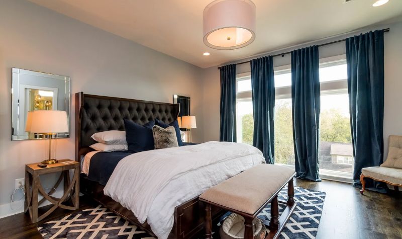 Floor to ceiling window with curtains and bed with bench in front and wooden side table