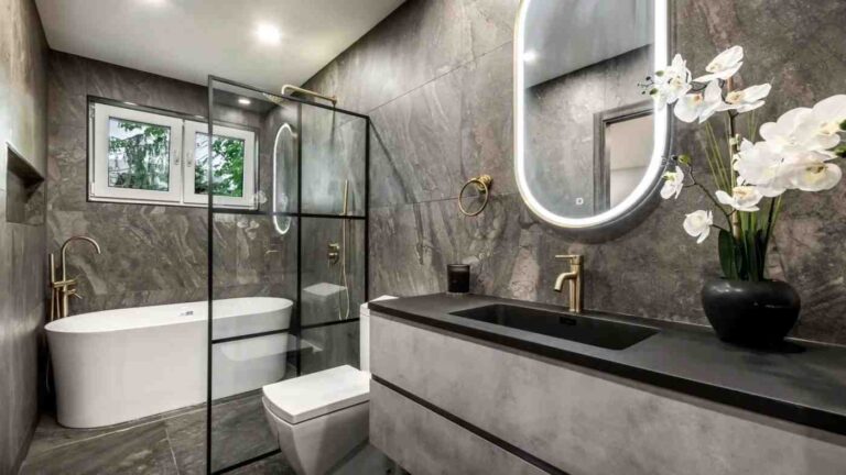 the-bathroom-with-grey-marble-style-walls-and-flooring-and-large-oval-LED-backlit-mirror
