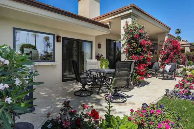 the-house-has-a-light-colored-exterior-and-sloped-roof-and-large-sliding-glass-doors-and-windows