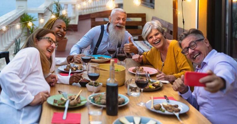 the-group-is-seated-around-a-wooden-table-with-plates-food-and-taking-picture