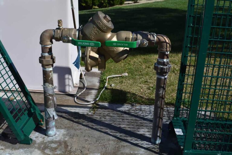outdoor-irrigation-backflow-prevention-device-installed-between-two-vertical-metal-pipes-and-device-is-mounted-above-the-ground-and-has-two-green-handled-valves