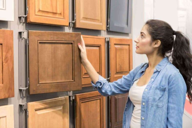 woman-standing-in-a-kitchen-cabinet-showroom-and-examining-different-cabinet-door-styles-displaced-on-a-wall