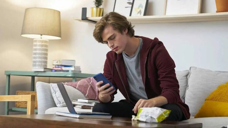a-young-man-in-a-hoodie-sitting-on-a-sofa-focused-on-his-smartphone-and-calculating-credit-score-for-home