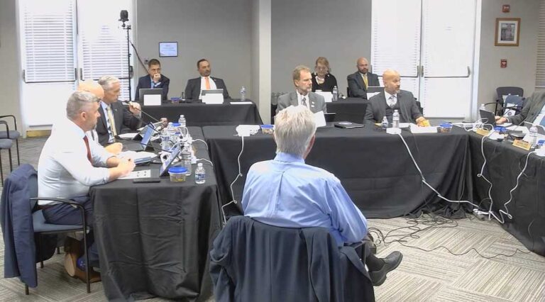 a-formal-public-meeting-likely-a-government-or-council-hearing-featuring-several-officials-seated-at-a-long-table