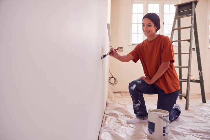 A Beginner’s Guide to Home Improvement Projects a-woman-is-shown-kneeling-while-applying-paint-to-a-wall-with-a-brush