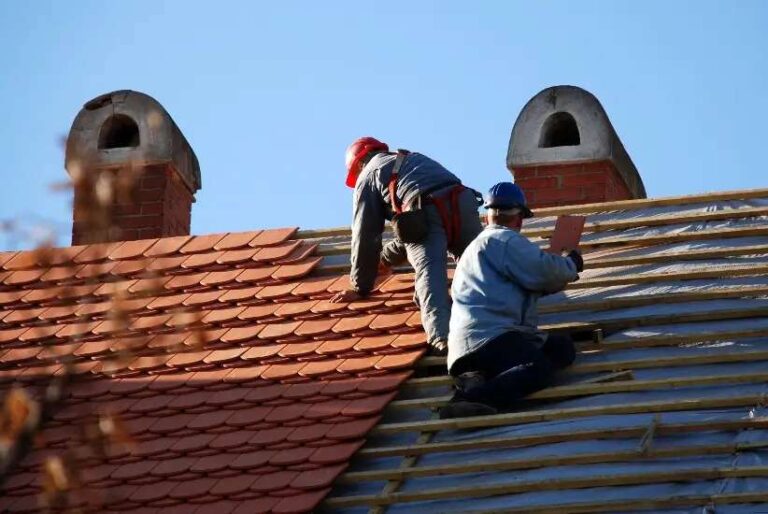 two-professional-roofers-working-on-a-residential-roof-during-a-clear-sunny-day-one-worker-is-installing-or-repairing-reddish-brown-roof