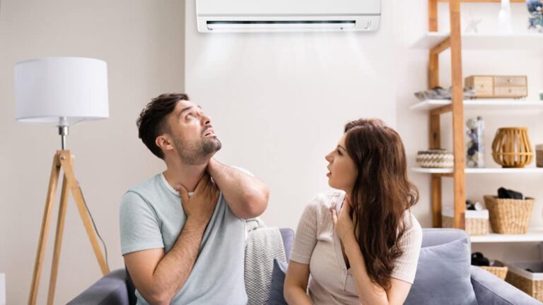 a-man-and-a-woman-sitting-on-a-gray-couch-indoor-appearing-physically-uncomfortable-due-to-poor-airflow-from-a-air-conditioner-above-them