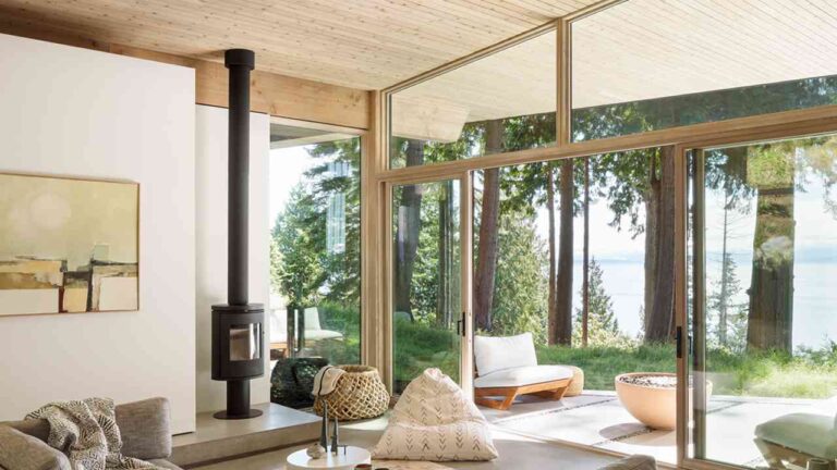 Blending Indoor Comfort with Outdoor Views: A Modern Home Approach a-modern-living-space-expansive-glass-walls-wrap-around-the-corner-of-the-room-to-provide-an-unobstructed-view-of-a-densely-wooded-evergreen-forest-outside