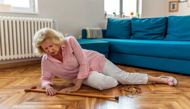 older-woman-on-the-floor-in-a-living-room-appearing-to-have-fallen-she-is-propped-up-on-arm-looking-distressed-and-holding-her-side-or-stomach