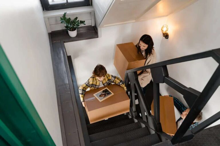 woman-and-a-child-carrying-cardboard-boxes-up-a-flight-of-stairs-in-a-home