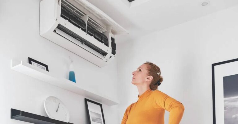 The Hidden Costs of Delaying Air Conditioning Repairs a-woman-is-looking-up-at-a-wall-mounted-split-system-air-conditioning-unit